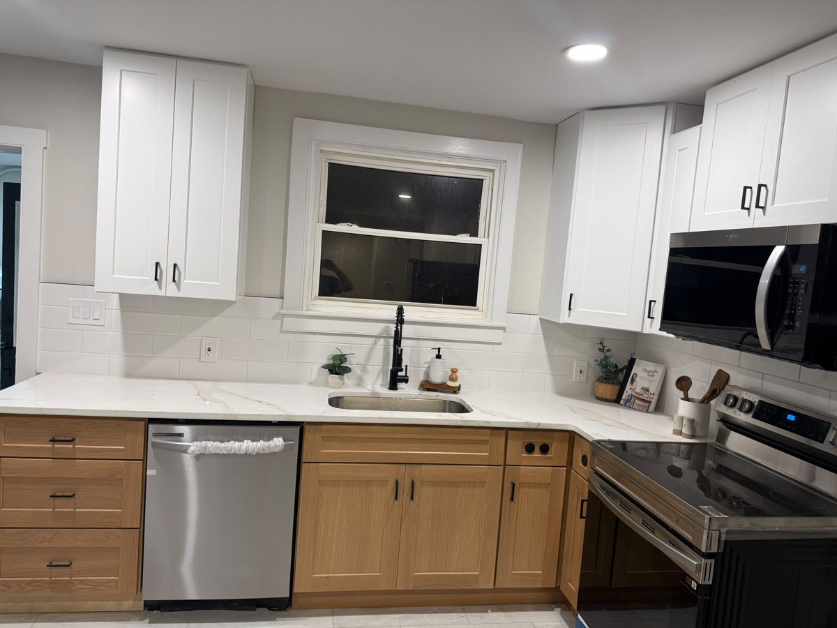 Remodeled kitchen with white shaker upper cabinets, oak base cabinets, quartz counters and a tiled floor
